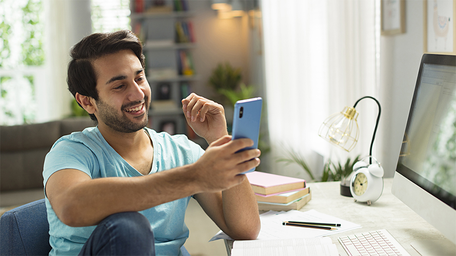 A man sitting on the beach with his mobile phone; image used for HSBC India Mobile banking page.