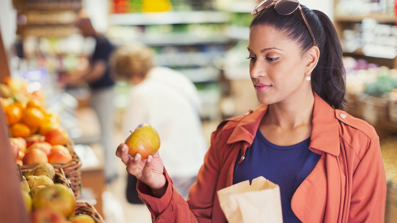 A woman holding an apple in a store; image used for HSBC compare NRI services page.