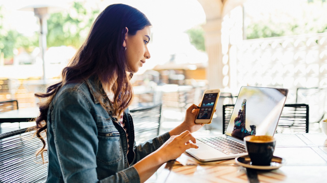 A woman using laptop and mobile at a café; image used for HSBC India Habits for financial wellbeing article