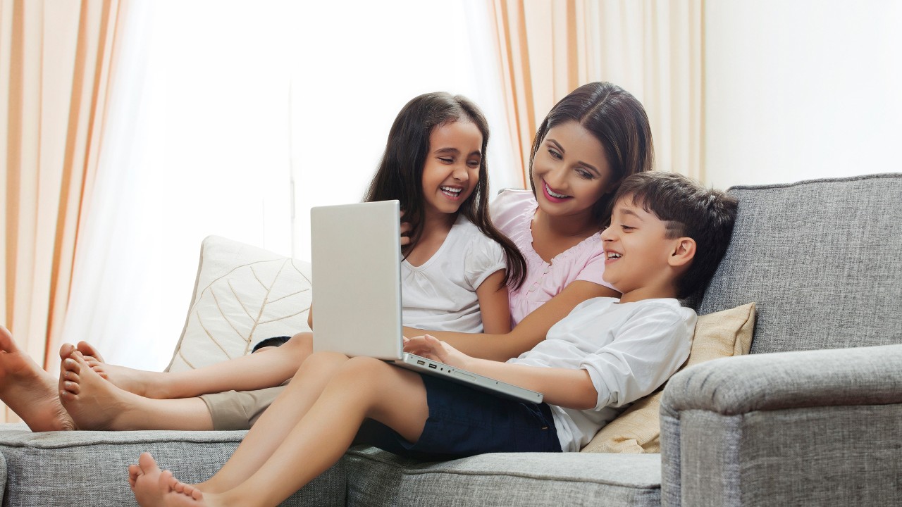 Mom and two kids happily using laptop on sofa; image used for HSBC India credit cards online offers