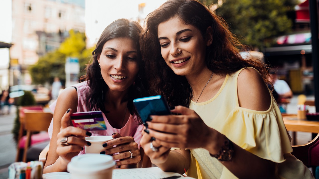 Two women at a cafe with a phone and a credit card; image used for HSBC Cashback Credit Card article page.