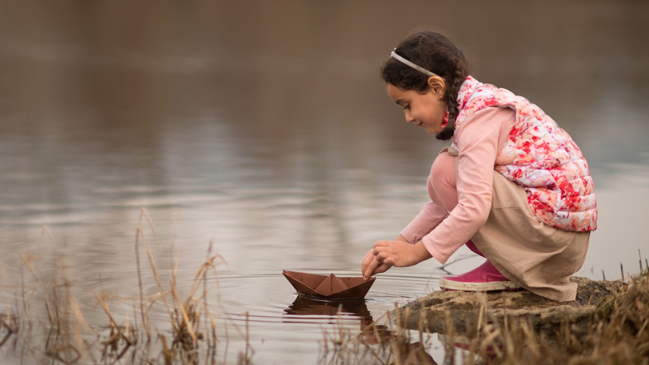 A little girl playing a boat near a river; image used for HSBC open Mariner’s account page