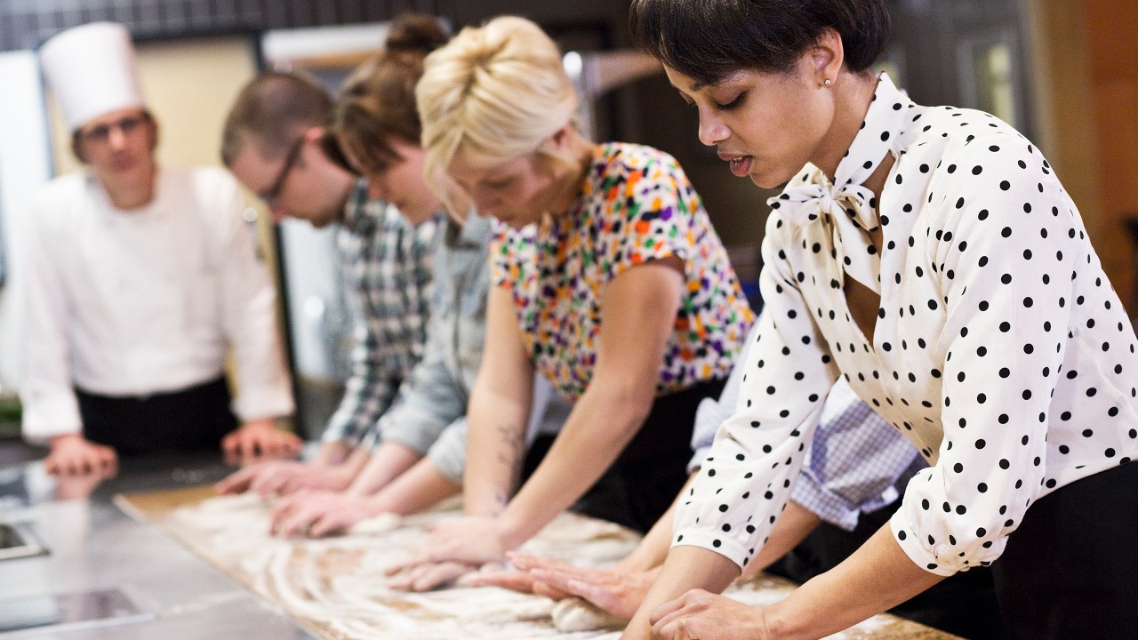 A male chef teaching a group of students to make stollen in a commercial kitchen; image used for 7 Great Ways to Use Extra Cash Page.