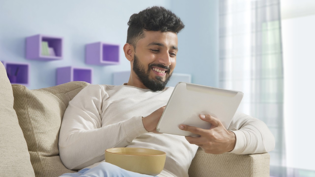 A man enjoy using tablet time at home; image used for HSBC JioFiber credit card offer