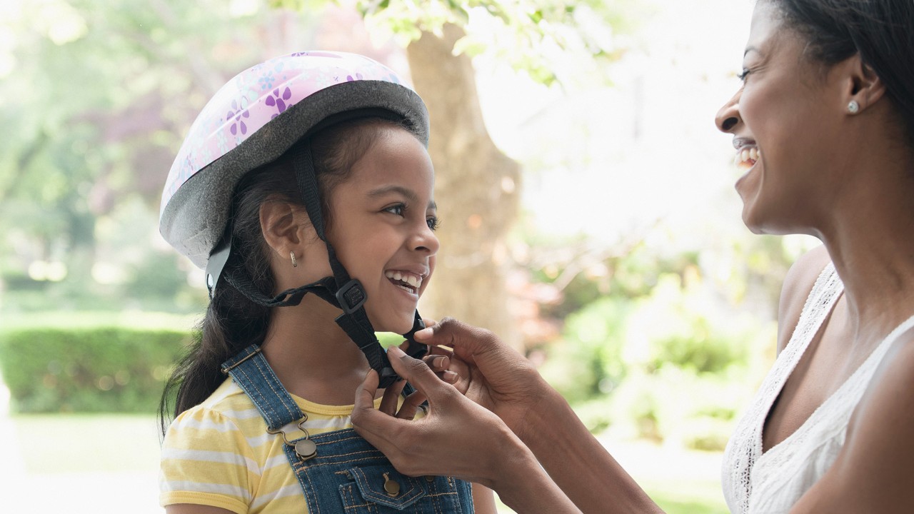 Woman fitting helmet on female child; image used for HSBC safeguard.