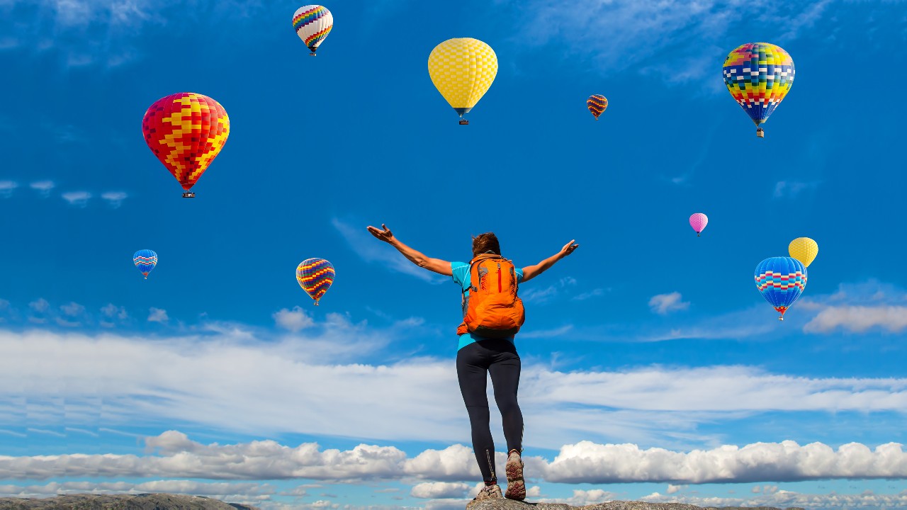 A woman with backpack looking up the hot air balloons in the sky; image used for HSBC India Premier emergency services page