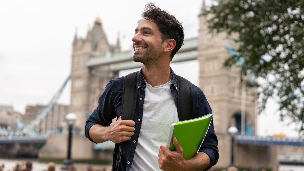 A young man with backpackers smiling under London bridge; image used for HSBC studying aboard.