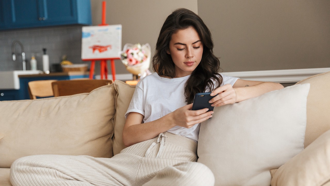 A woman using mobile relaxing at home; image used for HSBC IN debit card offer