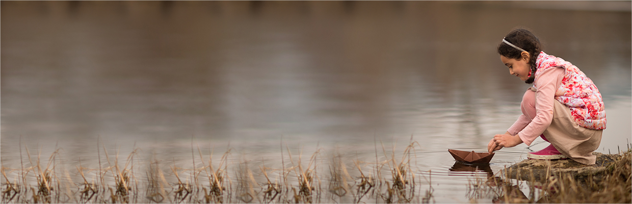 A little girl playing a boat near a river; image used for HSBC open Mariner’s account