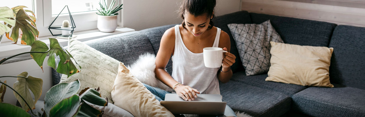 A woman using laptop with a coffee at home; image used for HSBC e-NACH