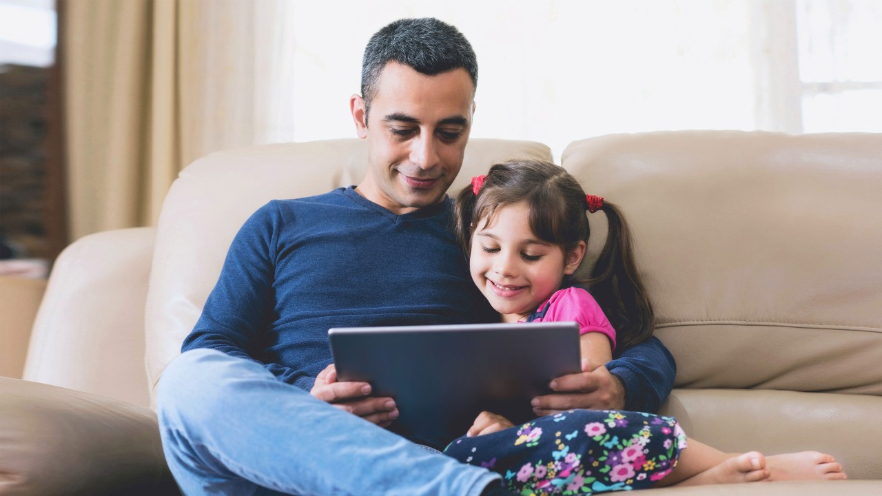 Father and little daughter looking at tablet on sofa; image used for HSBC India Credit Card limited time offer page