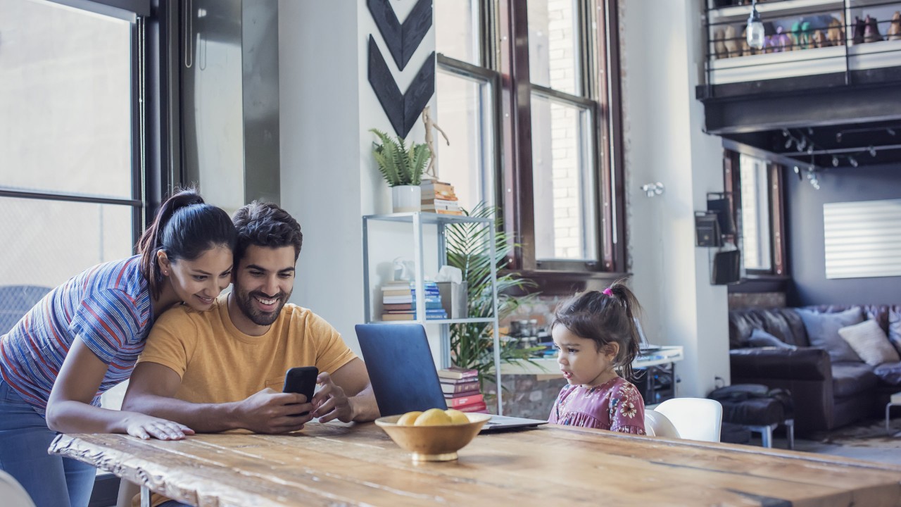 Parents looking at mobile and daughter looking at laptop in the living room